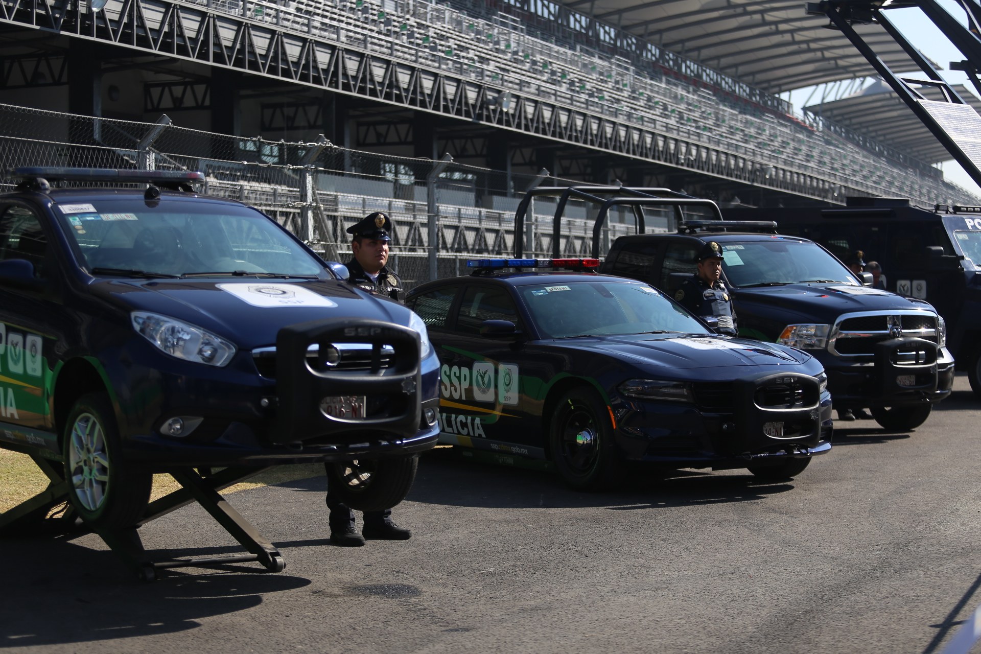 Polizeiautos vor einer Rennstrecke geparkt, mit uniformierten Personen, Stadion und Absperrung im Hintergrund.