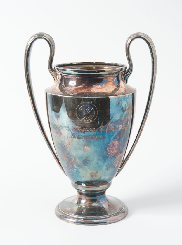 Der UEFA-Champions-League-Pokal, ein stählerner Becher mit zwei Griffen, in Blau und Silber gehalten, mit der Inschrift "UEFA Champions League", vor einem weißen Hintergrund dargestellt.