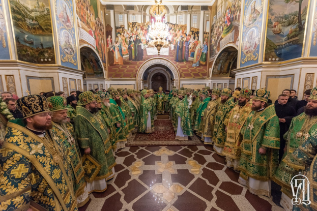 Gruppe von Priestern in grüner und goldener Gewandung, die in einer Kirche mit bemalten Wänden, einem Kronleuchter und einem Bogen im Hintergrund während einer St. Peters-Feier stehen.