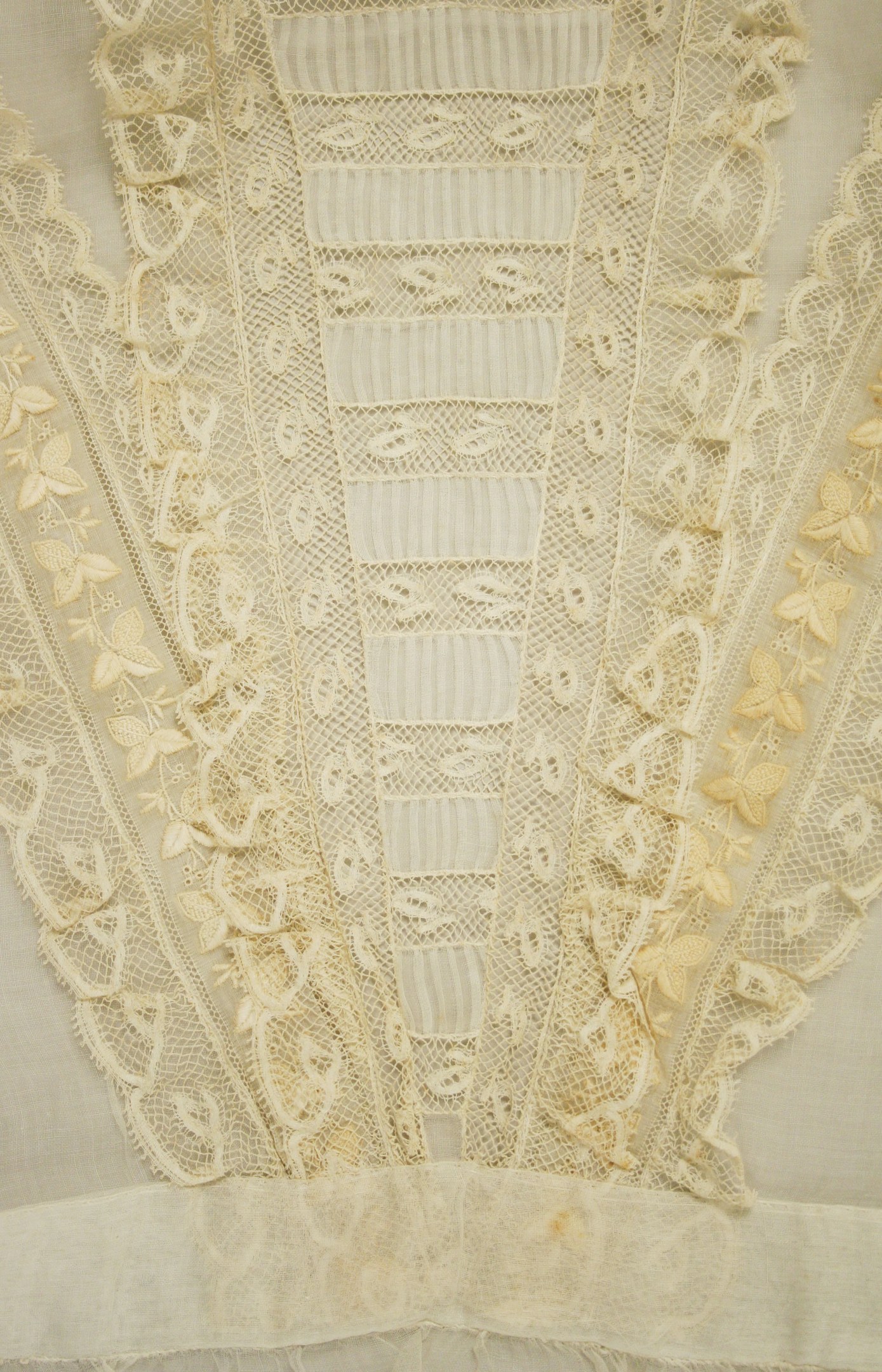 Nahaufnahme eines weißen Kleides mit zarter, detailreicher Spitzenverzierung, die verschiedene Muster und Formen zeigt, entworfen für einen leichten, luftigen Sommertag.
