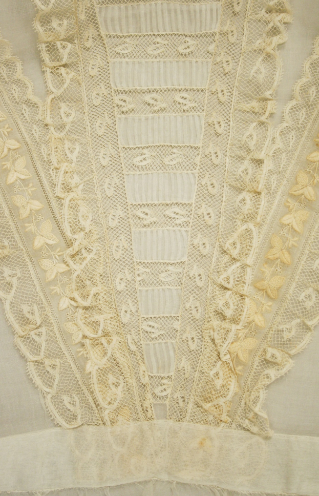 Nahaufnahme eines weißen Kleides mit zarter, detailreicher Spitzenverzierung, die verschiedene Muster und Formen zeigt, entworfen für einen leichten, luftigen Sommertag.