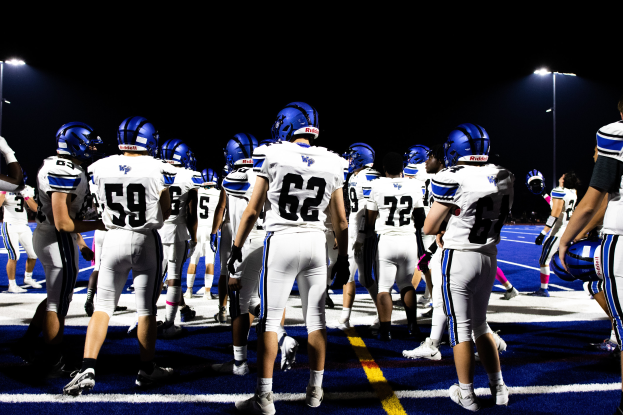 Eine Gruppe von Fußballspielern in Helmen und Stiefeln steht auf einem Feld, mit Flutlichtmasten im Hintergrund.
