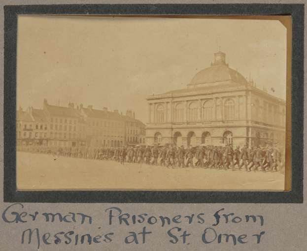 Deutsche Gefangene aus Messines vor einem Gebäude mit einem klaren blauen Himmel im Hintergrund, mit Text unten.