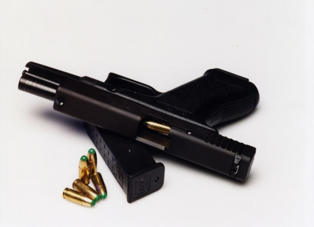 Schwarze Pistole mit geladenem Magazin und losen Patronen auf einer weißen Oberfläche.