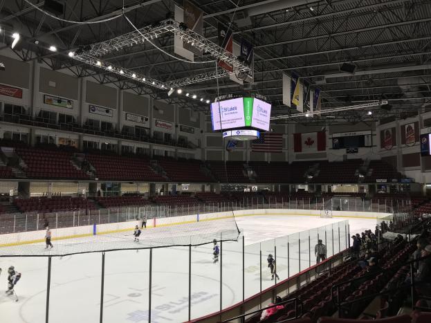Ein Eishockeyspiel in einer großen Arena mit einem Netz in der Mitte, Zuschauern auf beiden Seiten und Banner und Fahnen an den Wänden, identifiziert als St. Louis Blues Arena.