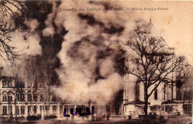 Schwarzes und weißes Foto eines brennenden Gebäudes mit Rauch aus Fenstern, umgeben von Bäumen und teilweisem Text oben.