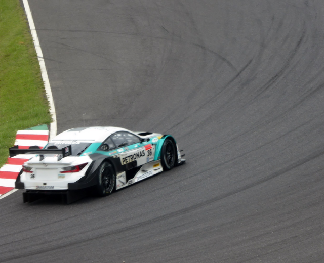 Ein silberner Mercedes-AMG GT3 Rennauto auf einer Rennstrecke mit Sponsorentext und Gras links.