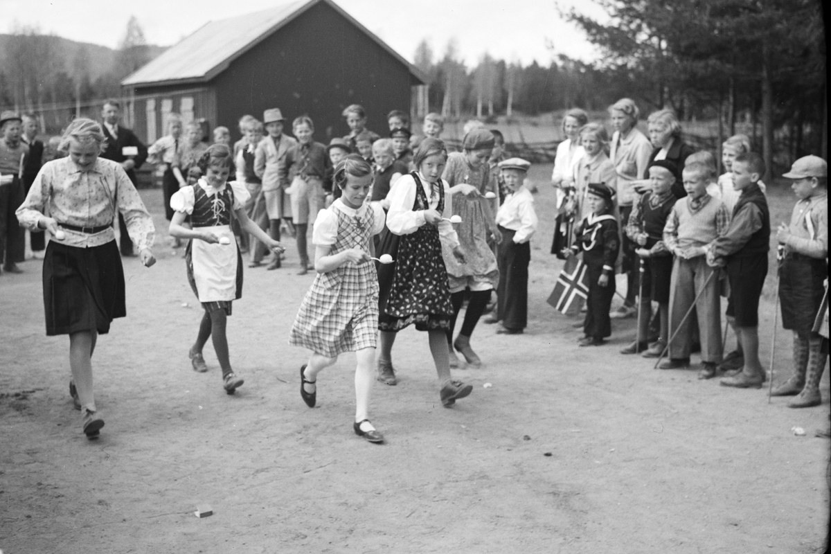 Schwarzes Bild von Kindern, die Fußball spielen, mit einer Menge, die Fahnen hält, Bäumen und einem Haus im Hintergrund.