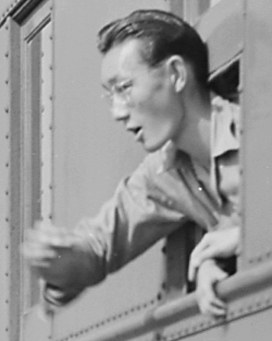 Schwarz-weißes Foto eines Mannes mit Brille, der ernst aus einem Zugfenster schaut und ein Hemd trägt.