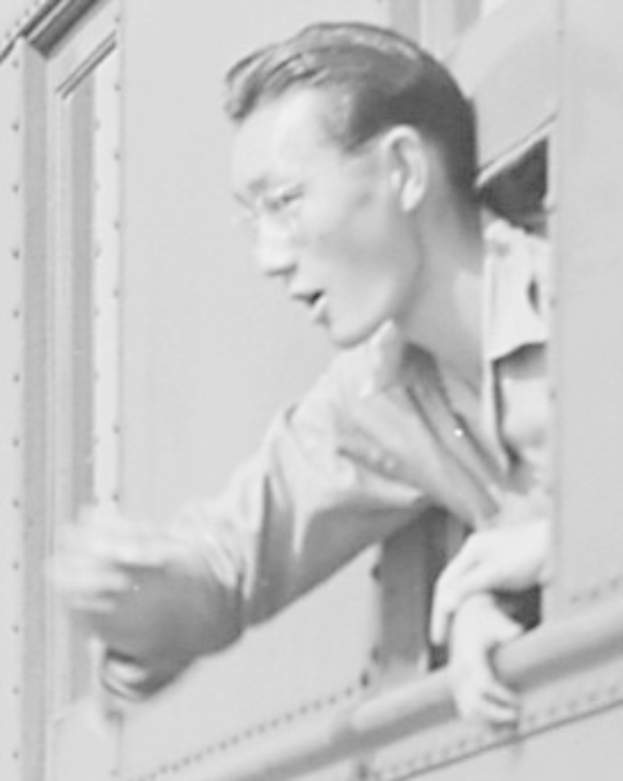 Schwarz-weißes Foto eines Mannes mit Brille, der ernst aus einem Zugfenster schaut und ein Hemd trägt.