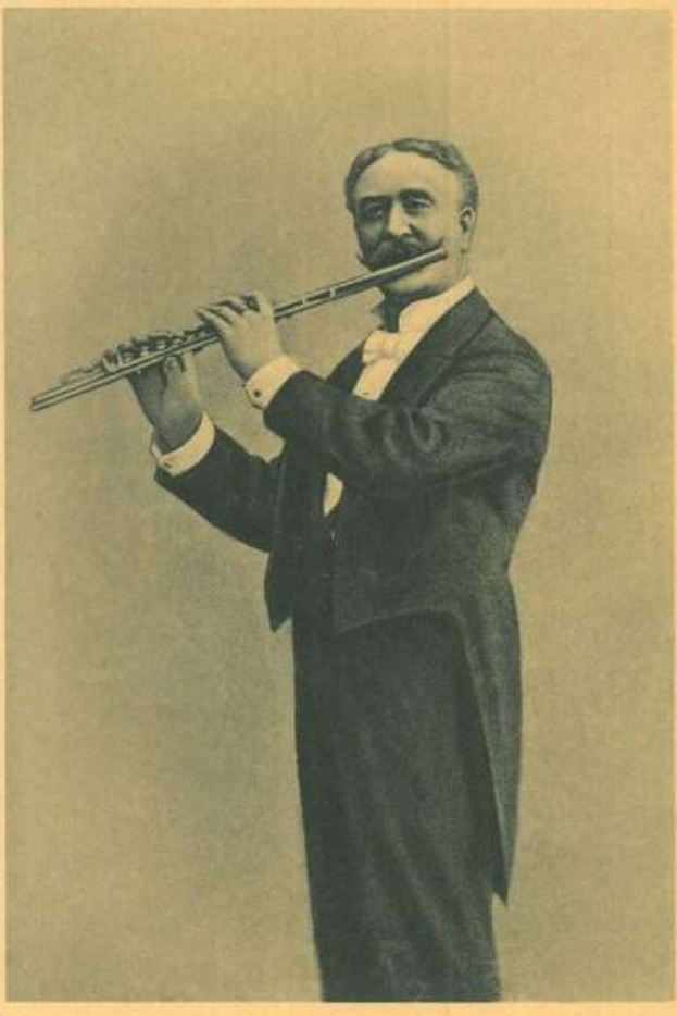 Altes Schwarz-Weiß-Foto eines Mannes in einem Smoking, der auf der Bühne eine Flöte spielt und dabei die Augen geschlossen hat.