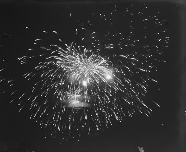 Schwarzes und weißes Foto von Feuerwerksexplosionen vor dunklem Nachthimmel.