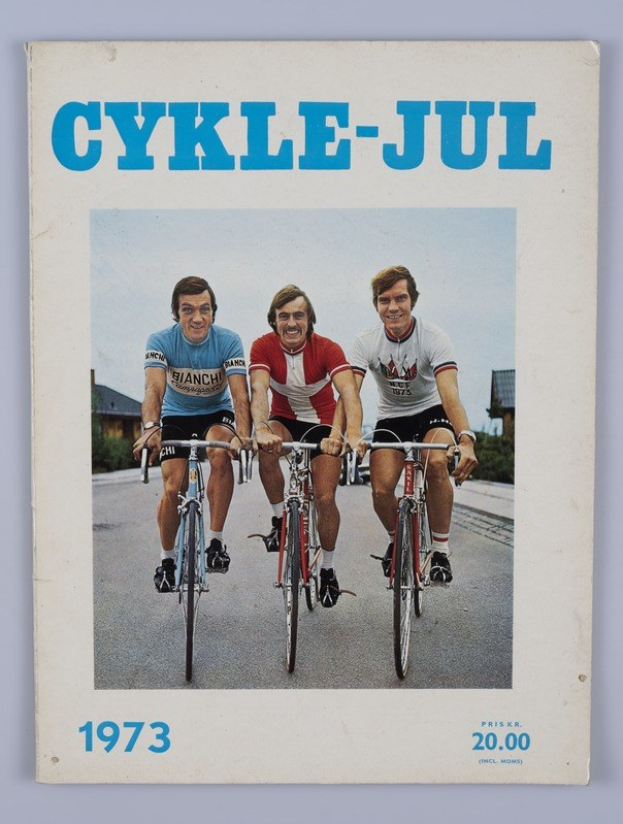 Drei Menschen, die Fahrräder auf einer Straße mit Häusern, Bäumen und einem klaren blauen Himmel fahren, mit dem Text "Cykle-Jul 1973 - Cyclocross Magazine" oben und unten.
