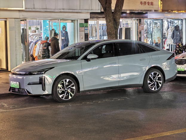 Elektrischer Mitsubishi Lancer EV auf einer nächtlichen Stadtstraße geparkt, umgeben von Gebäuden, Schaufenstern, Puppen und beleuchteten Schildern.