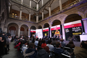 Eine Gruppe von Menschen, die an einem Tisch mit einem Podium und einem Mikrofon vor einer Menge, Kameras und Transparenten sitzt, was auf eine Pressekonferenz für das CDMX 2017-Event hindeutet.