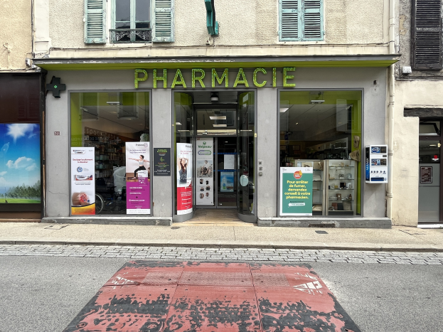 Apotheke mit Glaswänden und -türen, Plakate an den Innenwänden, befindet sich an einer Straßenkreuzung mit einer sichtbaren Straße unten.