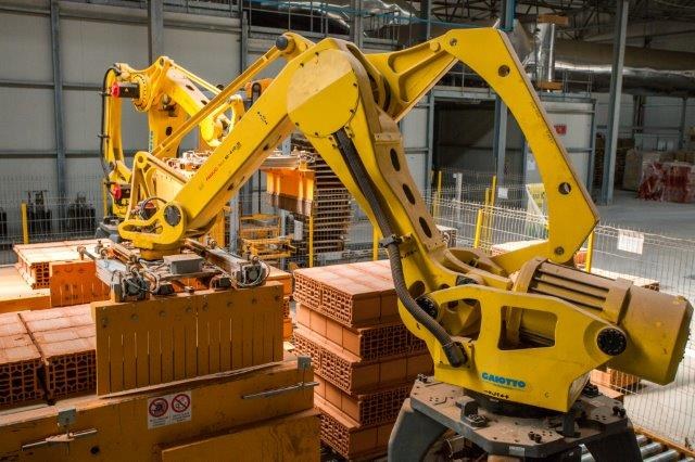 Industrielles Lagerhaus mit gestapelten Kisten, Kränen, Zäunen, Pfählen und einer fernen Wand in einer Fertigungseinrichtung.