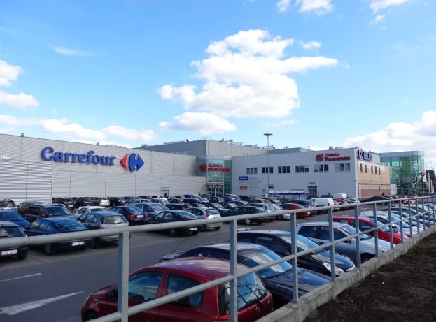 Großes Autohaus mit zahlreichen Fahrzeugen auf dem Hof, umgeben von Gebäuden und Straßeninfrastruktur unter einem bewölkten Himmel.