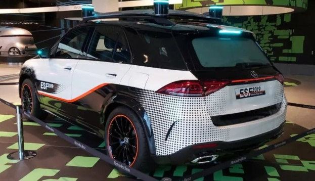 Mercedes-Benz E-Klasse Electric SUV auf der IAA in Frankfurt zu sehen, umgeben von Absperrpollern mit Seilen und Lichtern, mit einem anderen Fahrzeug und Text an einer Wand im Hintergrund.