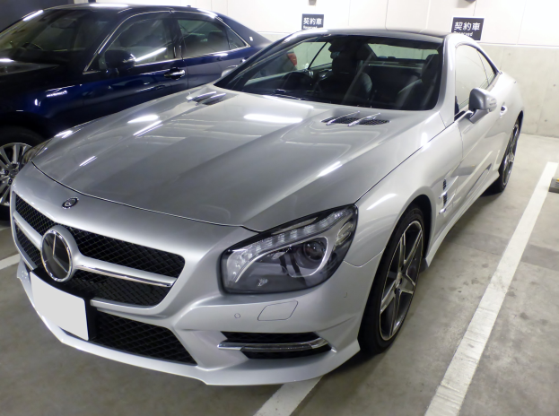 Silberner Mercedes-Benz SL-Class in einer Tiefgarage geparkt neben anderen Autos, mit Garagenwänden und Texttafeln im Hintergrund.