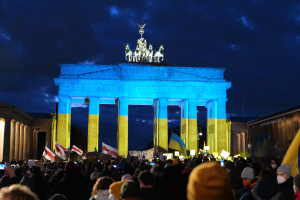 Eine Menschenmenge steht vor dem Brandenburger Tor in Berlin, Deutschland, mit Fahnen und Plakaten, mit einer Banner auf der rechten Seite.