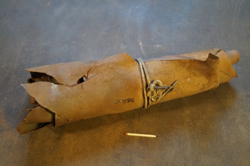 Ein brauner Papiertüte, die wie eine Granate aussieht, mit einem Seil verschnürt und auf einem Tisch platziert, mit einer Zigarette daneben.