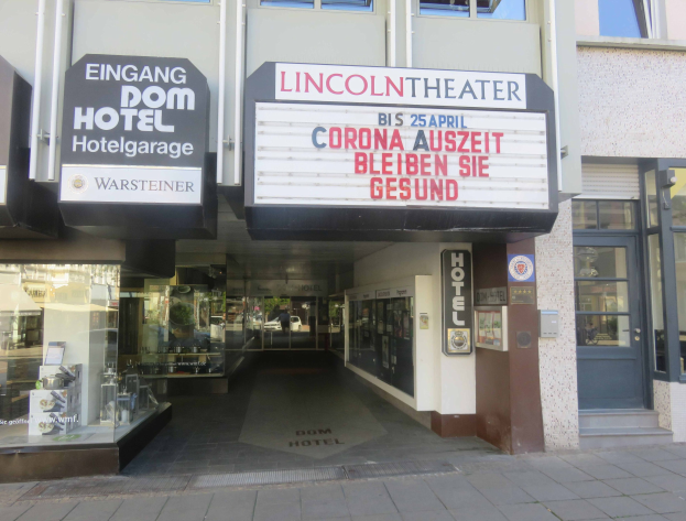 Außenansicht des Lincoln Theaters in Berlin, Deutschland, mit Glasfenstern und -türen sowie einer Tafel und einem Innenraum, der eine pulsierende Stadtlandschaft suggeriert.