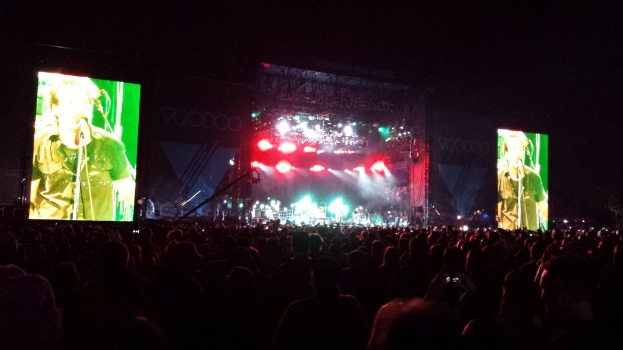 Bühne mit großer Menschenmenge darunter, flankiert von zwei großen Bildschirmen links und rechts.