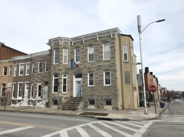 Eine Häuserreihe an einer Straßenecke in einem neuen Wohnprojekt in Philadelphia, mit Fenstern, Türen, Treppen mit Geländern, Laternen, Schildern und Fahrzeugen, mit Bäumen und einem bewölkten Himmel im Hintergrund.