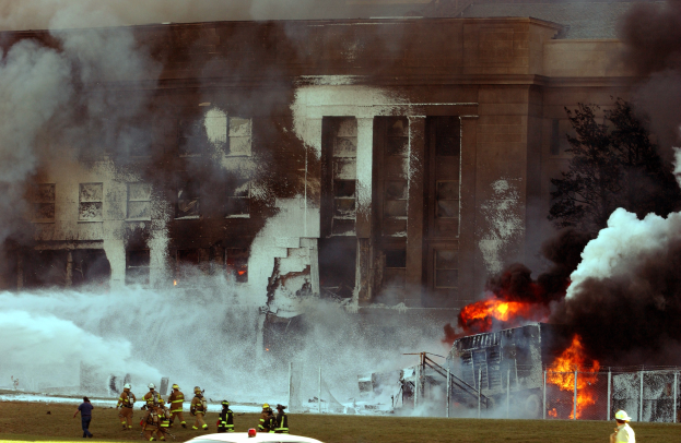Gro├če Halle steht in Flammen mit Feuerwehren, die aktiv dabei sind, das Feuer zu l├Âschen, Rauch steigt in den Himmel.