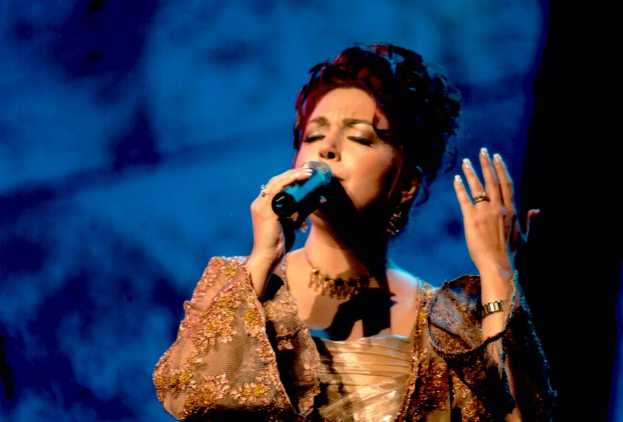 Frau in goldenem Kleid singt auf der Bühne der Eurovision Song Contest vor einem blauen und schwarzen Hintergrund.