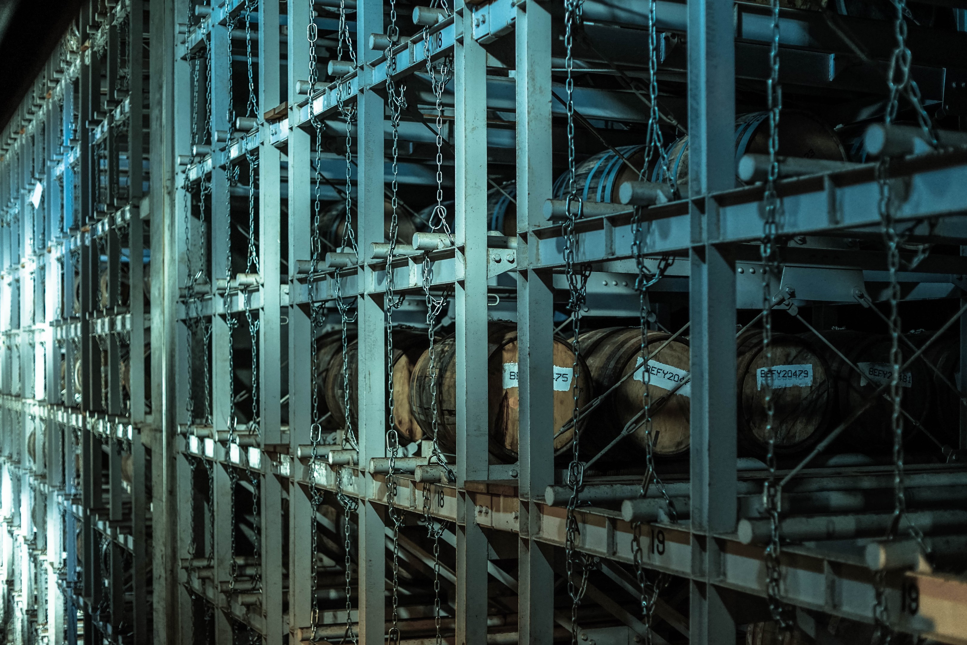 Ein großes Lager mit zahlreichen Fässern, die in geordneten Metallregalen gestapelt und durch Stangen und Ketten verbunden sind.