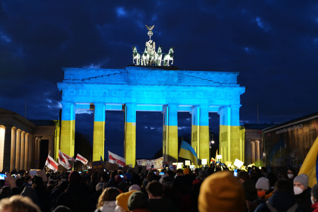 Eine Menschenmenge steht vor dem Reichstagsgebäude in Berlin und hält Fahnen und Schilder, auf denen ein protestbezogenes Textband zu sehen ist.