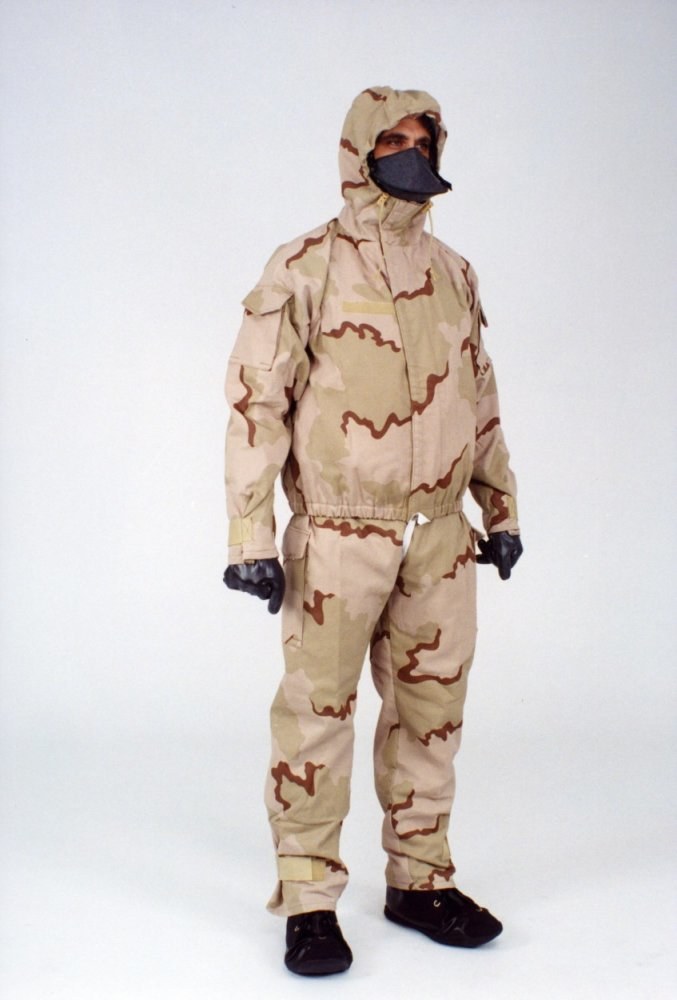 Ein Mann in einem Tarnmuster-Schutzoverall mit Kapuze und Maske steht vor einem weißen Hintergrund.