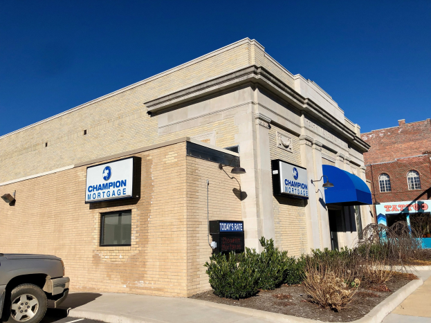 Gebäude mit "Champion Mortgage, Inc."-Schriftzug, geparktem Auto, Pflanzen, Bäumen und einem bewölkten Himmel.