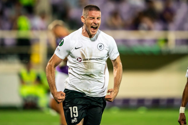 Ein Mann in weißem T-Shirt und schwarzen Shorts rennt auf einem Fußballfeld, umgeben von einer Gruppe von Menschen, die ein Tor während eines Spiels zwischen Leeds United und Melbourne Victory feiern.