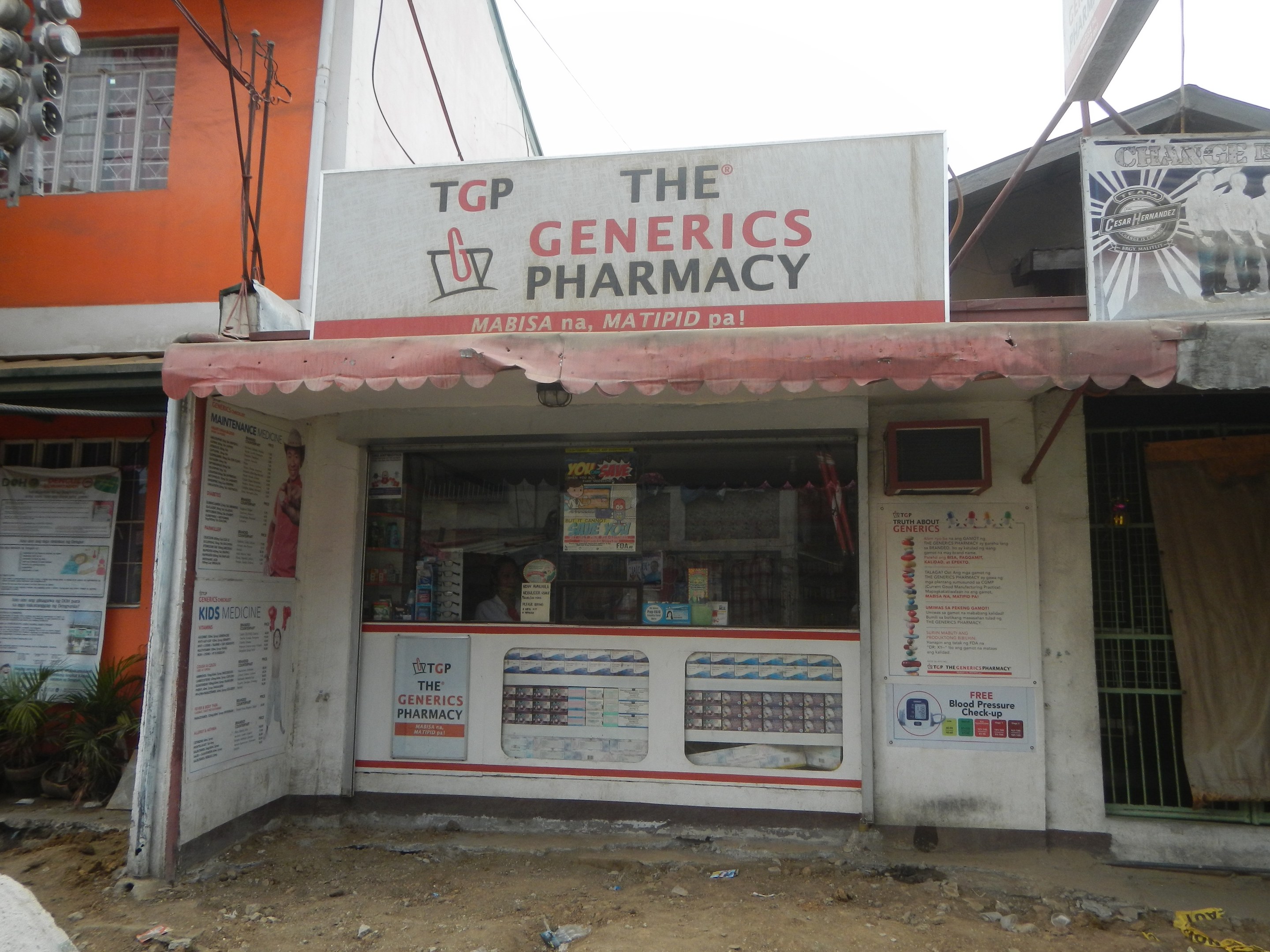 Außenansicht des "The Generics Pharmacy"-Ladens mit umliegenden stadtischen Elementen unter einem klaren blauen Himmel.