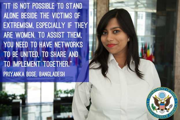 Eine Frau in einem weißen Hemd steht vor einem Gebäude mit einer Inschrift über Einheit und Unterstützung für Opfer von Extremismus, insbesondere Frauen, mit einem Logo in der rechten unteren Ecke.