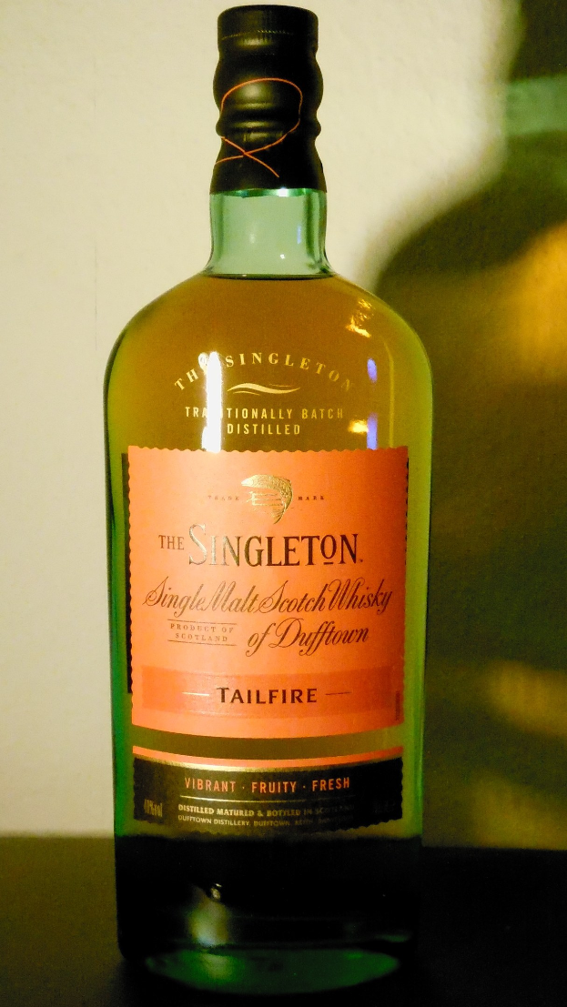 Eine tiefe bernsteinfarbene Flasche Singleton of Dufftown Tailfire Single Malt Scotch Whisky mit einem schwarzen Etikett, das ein Löwen- und Burgwappen zeigt.