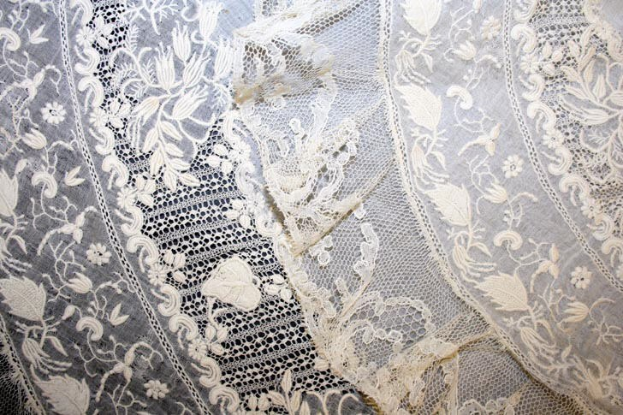 Nahaufnahme eines weißen Hochzeitskleids mit zarter, kunstvoller Spitzenverzierung und verschiedenen Mustern auf einem leichten, luftigen Stoff.