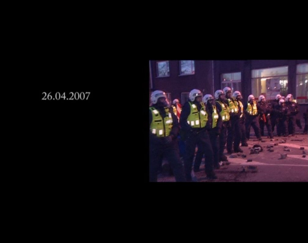 Gruppe von Polizisten in Helmen und Jacken vor einem Gebäude mit Fenstern stehend, mit einem Datum auf der linken Seite.