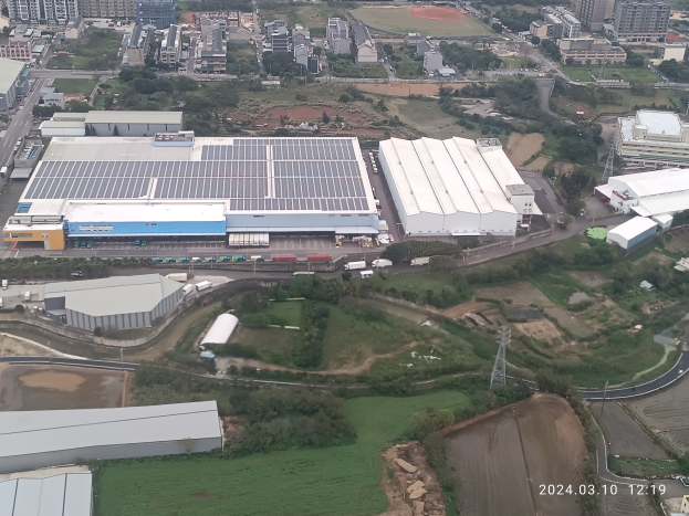 Eine Luftaufnahme eines großen Industriegebiets mit Gebäuden, Bäumen, Gras, Straßen, Fahrzeugen, Polen, Türmen und einem Wasserzeichen, das es sich um die erste Solarstromanlage in Singapur handelt, in der rechten unteren Ecke.