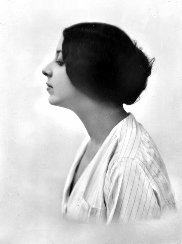 Ein Schwarz-Weiß-Foto einer Frau mit geschlossenen Augen, die ein Kleid trägt und eine 1920er-Jahre-Frisur hat, vor einem weißen Hintergrund.