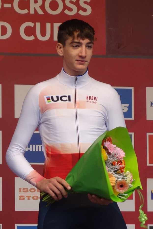 Ein Mann steht selbstbewusst auf einem Podium und hält einen Blumenstrauß, feiernd seinen Sieg.