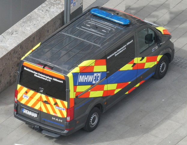 Ambulanzfahrzeug am Straßenrand mit einer Wand auf der linken Seite und einem sichtbaren Textschild.