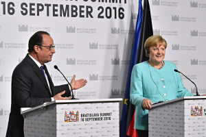 Bundeskanzlerin Angela Merkel und Frankreichs Präsident François Hollande vor zwei Podien mit Mikrofonen stehend, beide lächelnd, mit einem Banner "Bratislava Gipfel 2016" im Hintergrund.