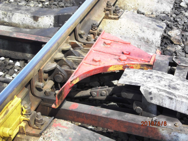 Nahaufnahme einer Eisenbahnschiene mit einer Metallschutzvorrichtung und Schottersteinen.