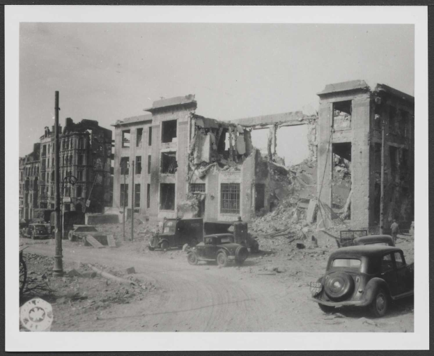 Schwarzes und weißes gerahmtes Foto eines zerstörten Gebäudes mit parkenden Autos davor, wahrscheinlich aufgenommen nach einem Bombenangriff in Berlin, Deutschland.