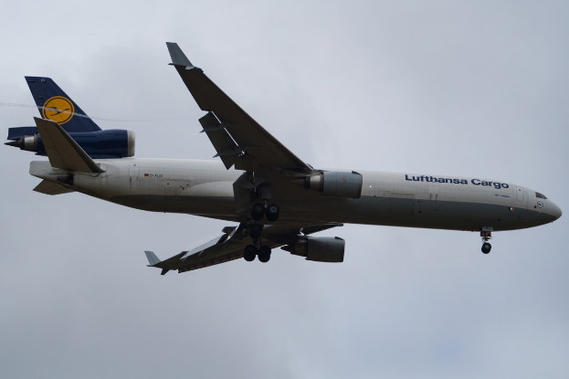 Eine Lufthansa Cargo Boeing 777-300ER im Flug, mit ausgebreiteten Tragflächen und aktivierten Triebwerken, mit sichtbarem Text auf dem Rumpf gegen einen bewölkten Himmel.