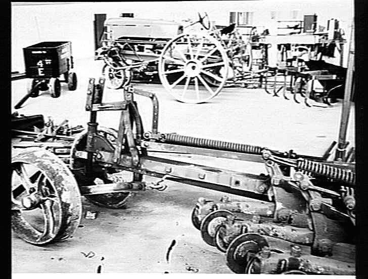 Schwarz-weißes Foto eines Traktors in einer Fabrik, mit einer Egge im Vordergrund und einer Wand im Hintergrund, eingerahmt von einem Rahmen.